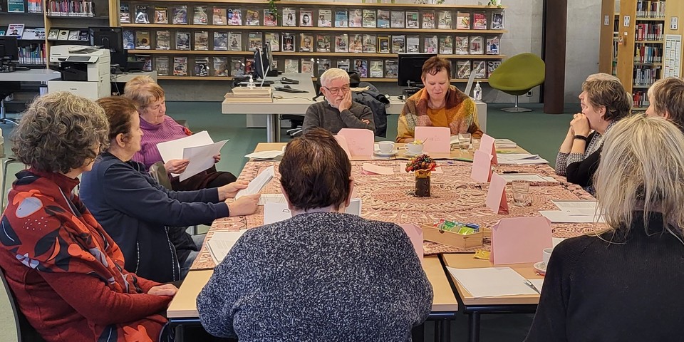 Een groep mensen rond een grote tafel die samen teksten lezen